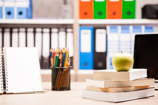 Green apple on pile of books next to a notebook and pencils on t